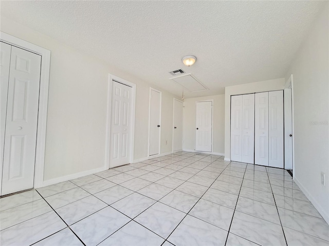 unfurnished bedroom featuring a textured ceiling, visible vents, baseboards, two closets, and attic access