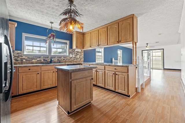 kitchen with light wood finished floors, a kitchen island, stainless steel fridge with ice dispenser, a sink, and backsplash