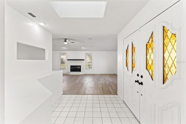 entrance foyer featuring light tile patterned floors, visible vents, a tiled fireplace, ceiling fan, and a textured ceiling