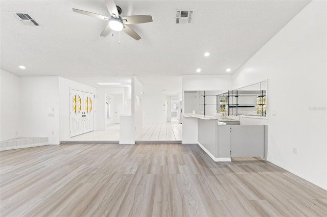 unfurnished living room featuring light wood-type flooring, ceiling fan, visible vents, and a textured ceiling