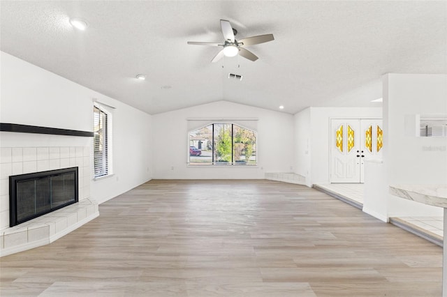 unfurnished living room with lofted ceiling, a textured ceiling, a tile fireplace, light wood-style flooring, and a ceiling fan