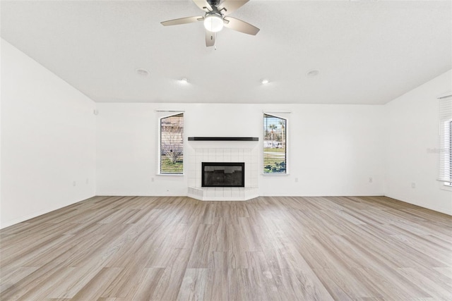 unfurnished living room with a tile fireplace, plenty of natural light, and light wood-style flooring