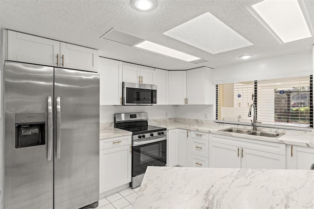 kitchen with light stone countertops, white cabinetry, stainless steel appliances, and a sink