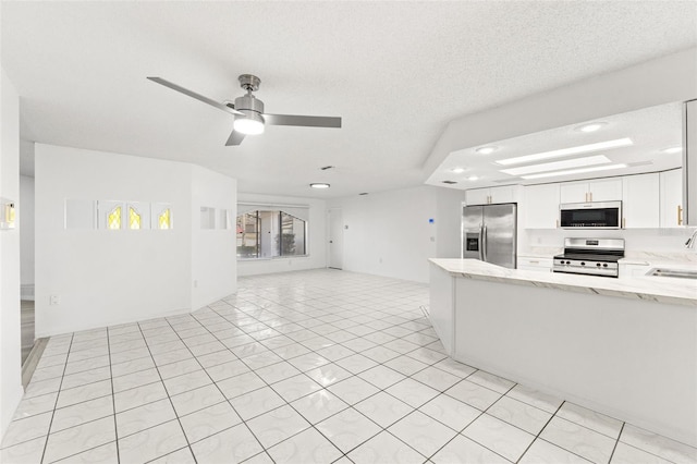 kitchen featuring open floor plan, appliances with stainless steel finishes, white cabinets, and light stone countertops