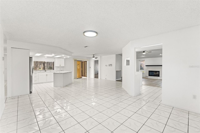 unfurnished living room with ceiling fan, light tile patterned floors, a textured ceiling, and a fireplace