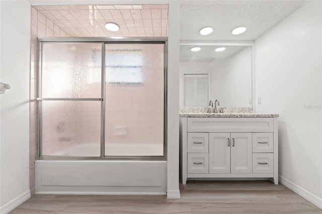 bathroom with combined bath / shower with glass door, wood finished floors, vanity, and baseboards