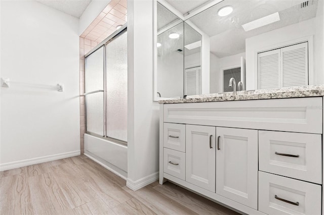 full bath with wood finished floors, vanity, baseboards, and bath / shower combo with glass door