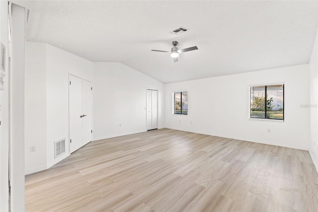 spare room featuring lofted ceiling, light wood-type flooring, visible vents, and a textured ceiling