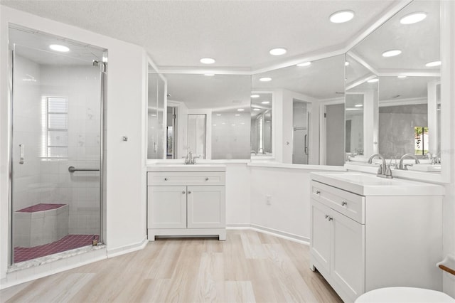 full bathroom with wood finished floors, two vanities, a sink, and a shower stall