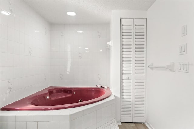 bathroom featuring a textured ceiling, a tub with jets, a closet, and tile walls