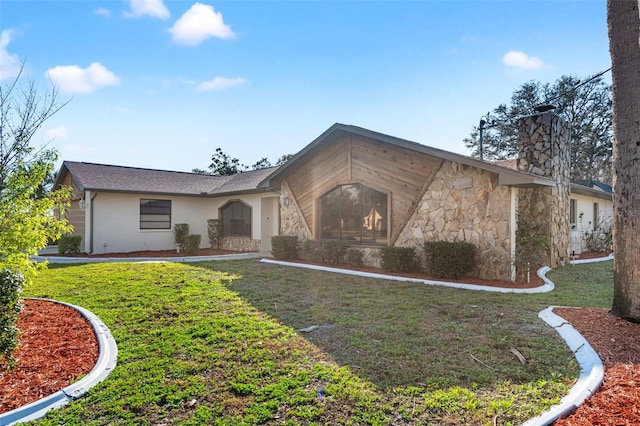 view of front of home featuring stone siding, a front lawn, a chimney, and stucco siding