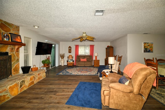 living room featuring a textured ceiling, ceiling fan, a stone fireplace, wood finished floors, and visible vents