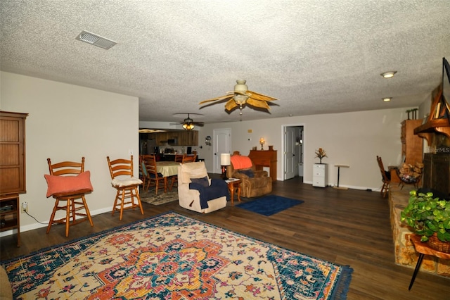 living area with baseboards, visible vents, a fireplace with raised hearth, and wood finished floors