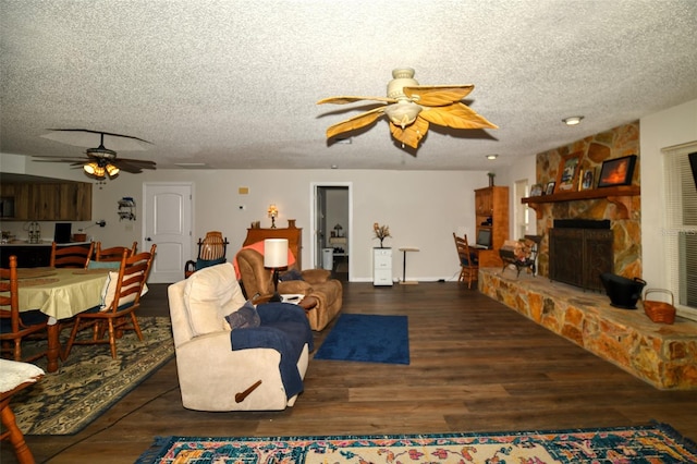 living area featuring ceiling fan, a textured ceiling, wood finished floors, and a stone fireplace