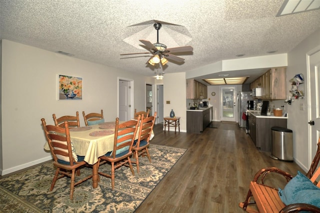 dining area featuring visible vents, dark wood-type flooring, a ceiling fan, a textured ceiling, and baseboards