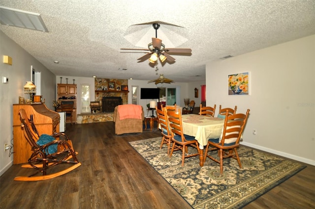 dining space with visible vents, a stone fireplace, a textured ceiling, and wood finished floors