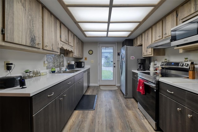 kitchen with under cabinet range hood, appliances with stainless steel finishes, light countertops, and a sink