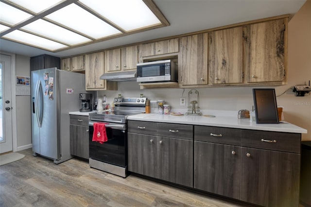 kitchen featuring under cabinet range hood, light wood-style floors, stainless steel appliances, and light countertops