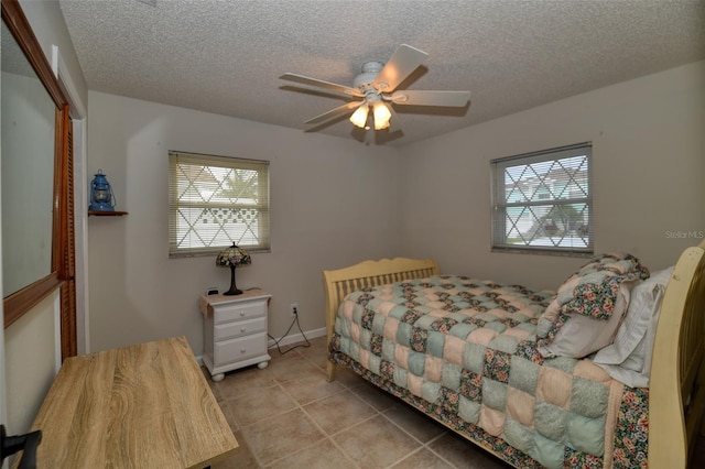 tiled bedroom with ceiling fan, multiple windows, and a textured ceiling