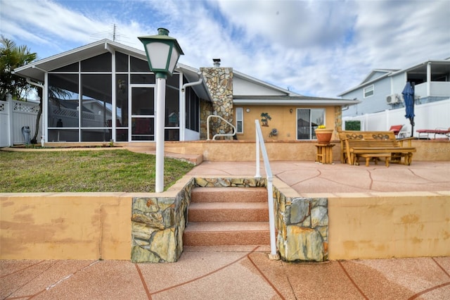 view of front of property featuring a patio, a sunroom, a chimney, fence, and a front lawn