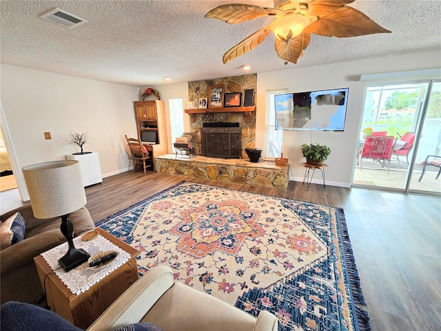 living area with a textured ceiling, a stone fireplace, baseboards, wood finished floors, and visible vents