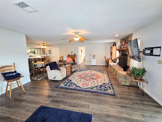 living room with a textured ceiling, ceiling fan, visible vents, and wood finished floors