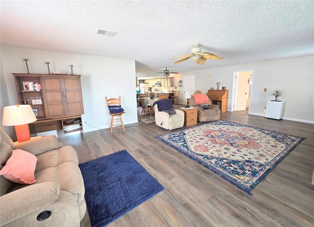 living room with visible vents, wood finished floors, baseboards, a textured ceiling, and a ceiling fan