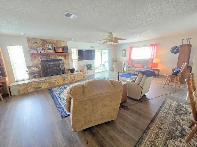 living area featuring a ceiling fan, a textured ceiling, visible vents, a fireplace, and wood finished floors