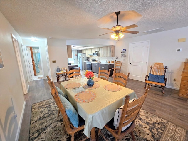 dining space with a ceiling fan, a textured ceiling, visible vents, dark wood finished floors, and baseboards