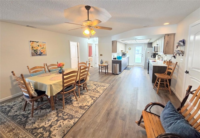 dining area with a textured ceiling, a ceiling fan, baseboards, wood finished floors, and visible vents