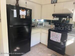 kitchen featuring tasteful backsplash, light countertops, under cabinet range hood, and black appliances