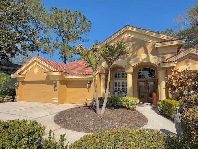 mediterranean / spanish home featuring an attached garage, concrete driveway, a tiled roof, french doors, and stucco siding