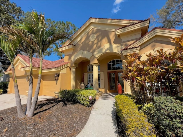 view of front of house featuring french doors, a tile roof, stucco siding, an attached garage, and driveway