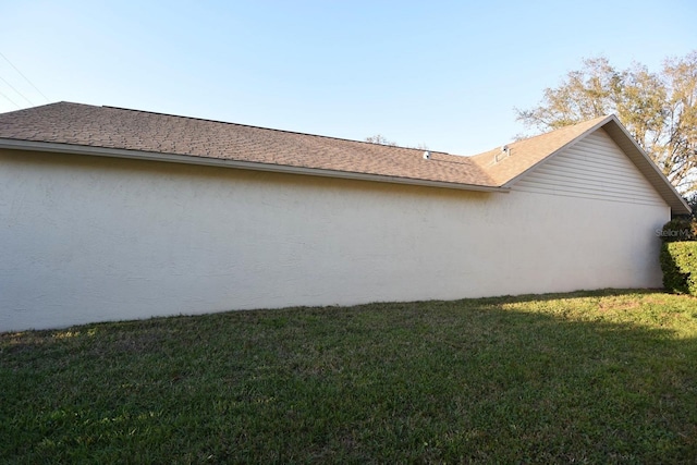 view of side of property featuring a shingled roof, a yard, and stucco siding