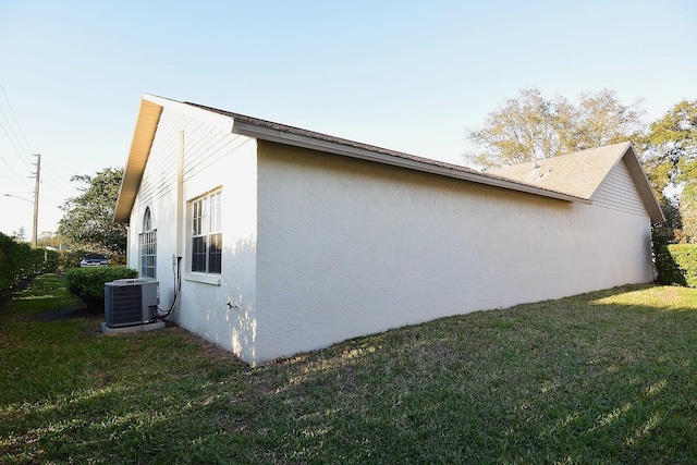 view of side of home featuring stucco siding, a yard, and central air condition unit