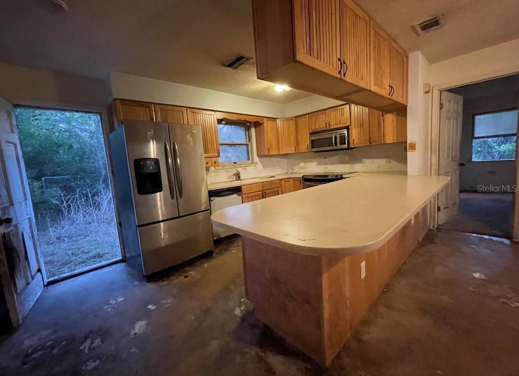 kitchen with visible vents, unfinished concrete flooring, a peninsula, stainless steel appliances, and light countertops