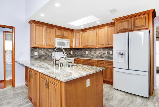 kitchen with white appliances, a skylight, brown cabinets, and light stone counters