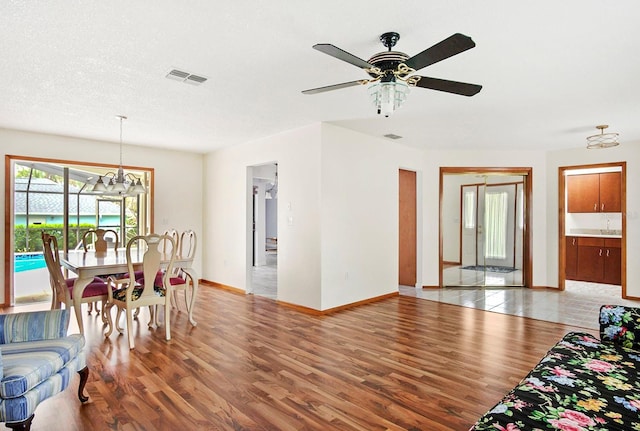 living room with light wood-style floors, baseboards, visible vents, and ceiling fan with notable chandelier