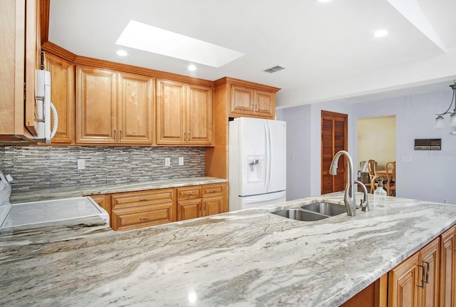 kitchen with white appliances, a skylight, a sink, visible vents, and light stone countertops