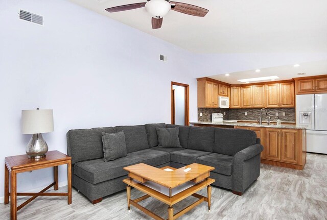 living room with a ceiling fan, lofted ceiling, visible vents, and light wood finished floors