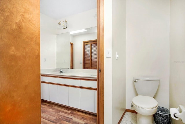 bathroom with double vanity, baseboards, toilet, wood finished floors, and a sink