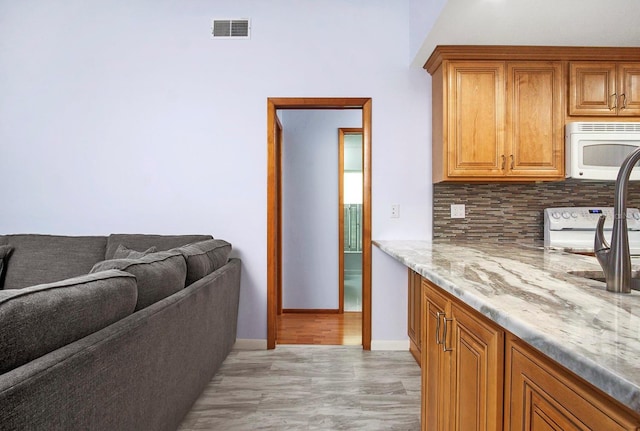 kitchen featuring brown cabinets, light wood finished floors, visible vents, backsplash, and white appliances