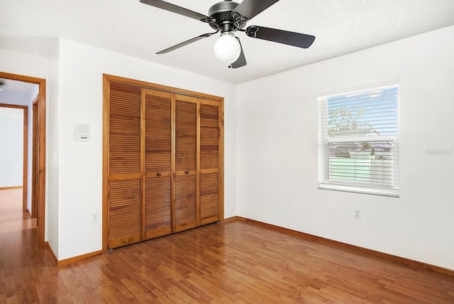 unfurnished bedroom with a closet, a ceiling fan, a textured ceiling, wood finished floors, and baseboards