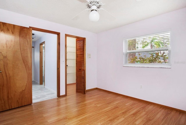 unfurnished bedroom featuring a walk in closet, a closet, light wood-style floors, ceiling fan, and baseboards