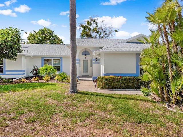 single story home featuring roof with shingles, a front yard, and stucco siding