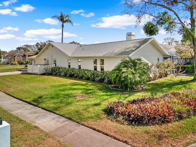 view of front of home featuring stucco siding, roof with shingles, a chimney, and a front yard