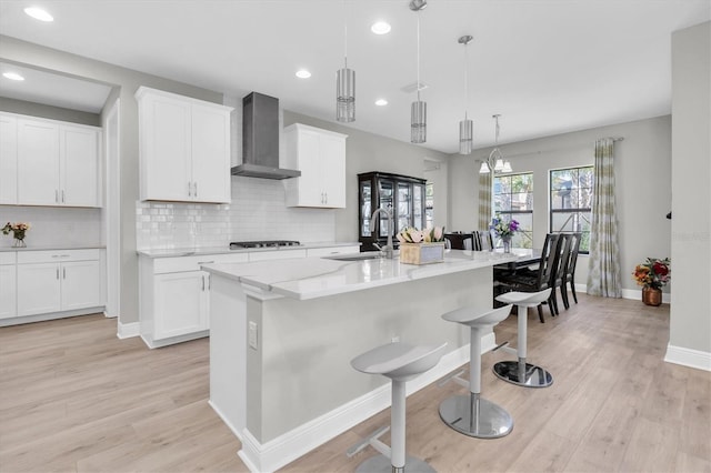 kitchen featuring a breakfast bar, a sink, light wood-style floors, wall chimney exhaust hood, and stovetop