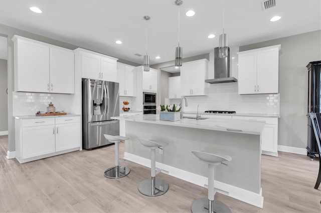 kitchen featuring stainless steel appliances, a sink, wall chimney range hood, light wood-type flooring, and a kitchen breakfast bar