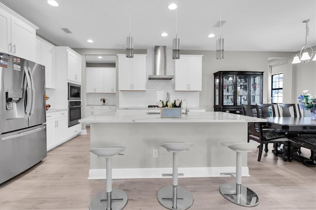 kitchen with a breakfast bar area, stainless steel appliances, visible vents, backsplash, and wall chimney range hood