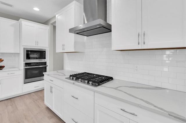 kitchen with white cabinetry, wall chimney range hood, visible vents, and appliances with stainless steel finishes